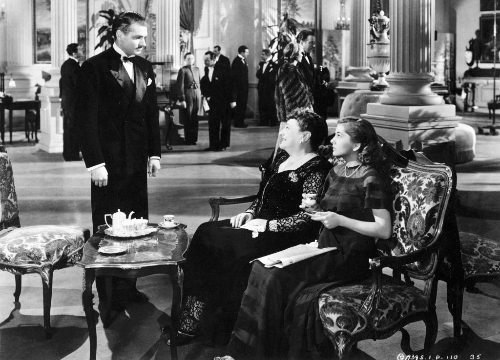 In Monte Carlo, Max de Winter (Laurence Olivier) stops to speak to Mrs. Edythe Van Hopper (Florence Bates) only after recognizing her companion (Joan Fontaine), the girl he had encountered earlier.  From "Rebecca"